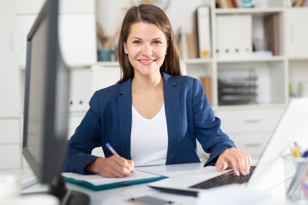 Porträt eines selbstbewussten lächelnden weiblichen Büroangestellten bei der täglichen Arbeit mit Laptop und Dokumenten